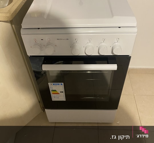 תנור גז לבן עם כפתורים ומדבקת אנרגיה